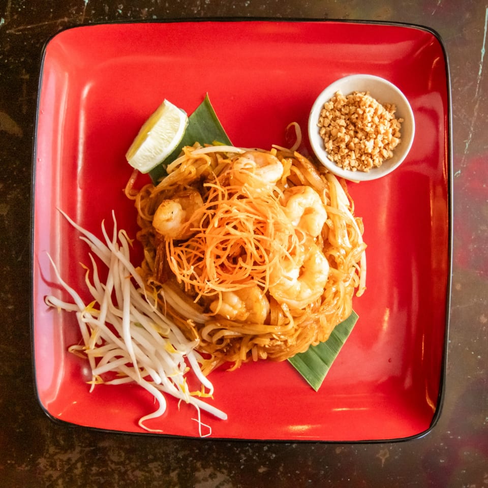 Shrimp Pad Thai with bean sprouts, lime, and crushed peanuts on a red plate.
