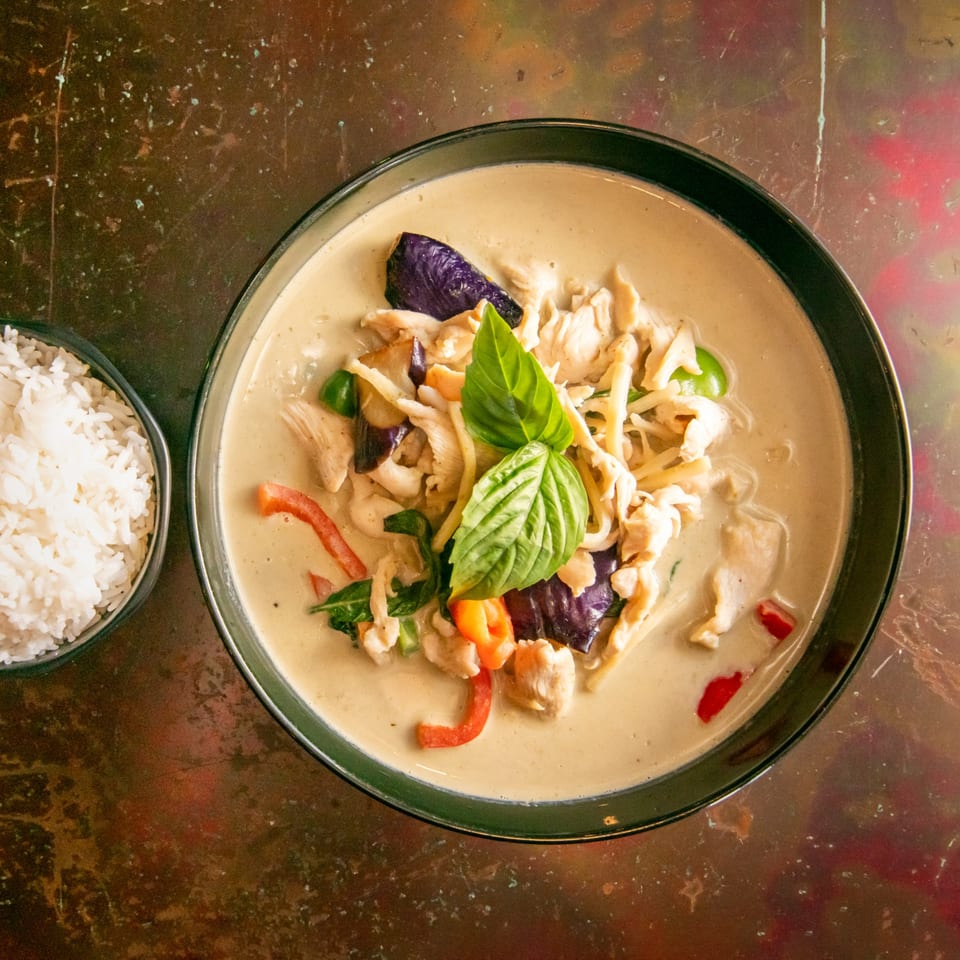 Overhead view of a bowl of green curry with chicken, eggplant, and basil, served with white rice.