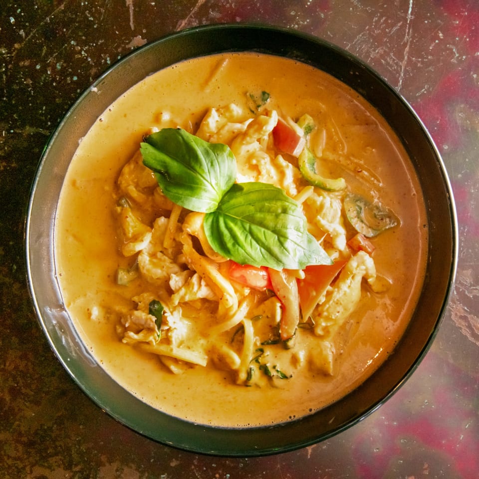 Overhead view of a bowl of red curry with chicken, vegetables, and basil leaves.
