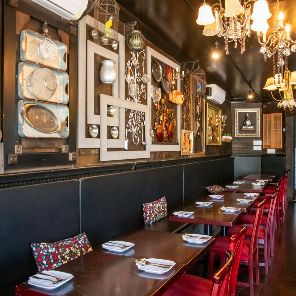 Restaurant interior with black booths, red chairs, dark tables set with plates, and decorative wall art.