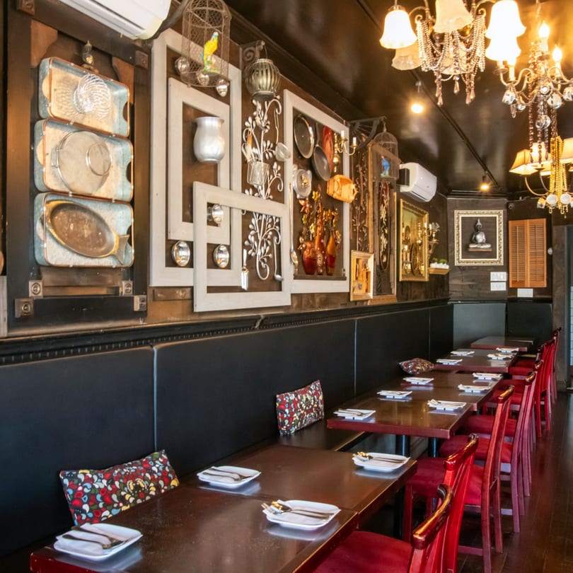 Restaurant interior with black booths, red chairs, dark tables set with plates, and decorative wall art.