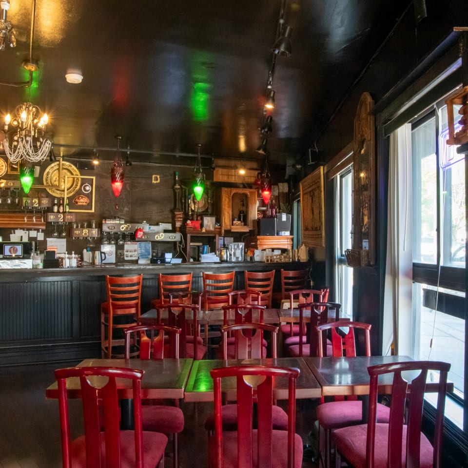 Restaurant interior with red chairs and tables, a bar, and decorative lighting.