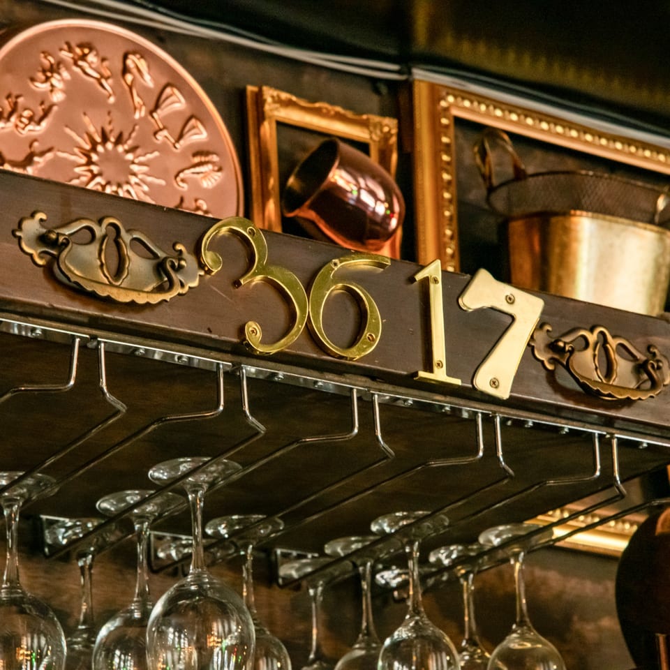 Golden numbers "3617" on a dark wooden shelf with hanging wine glasses and decorative items.