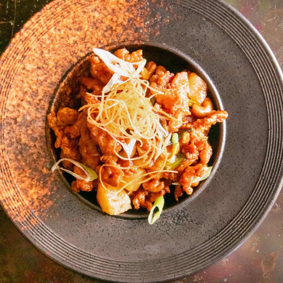 Sweet and sour chicken with cashews, pineapple, and scallions in a dark bowl.