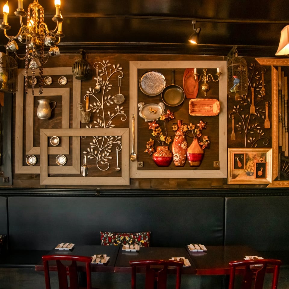 Restaurant interior with dark wood paneling, decorative kitchenware, and set tables with red chairs.