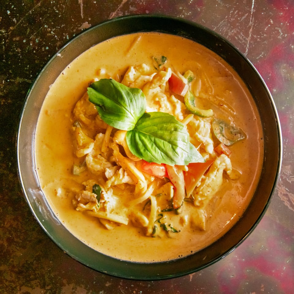 Overhead view of a bowl of red curry with chicken, vegetables, and a basil garnish.