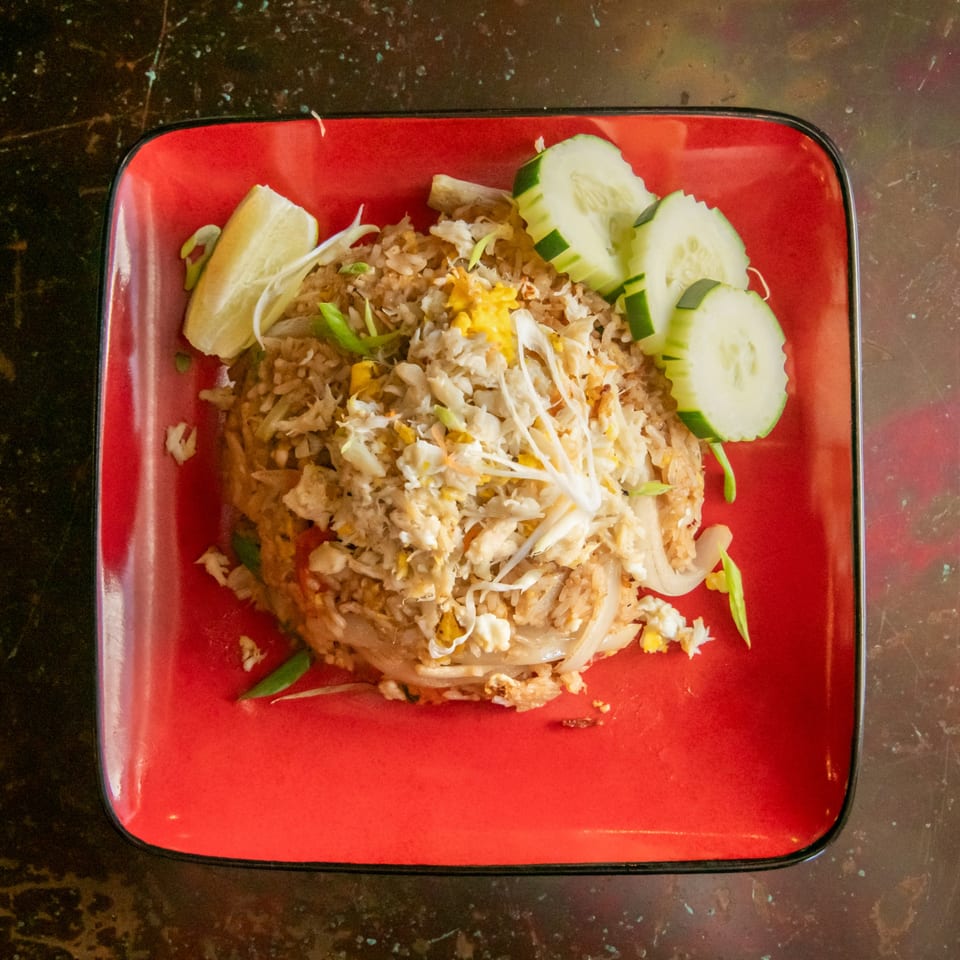 Crab fried rice with lime and cucumber slices on a red square plate.