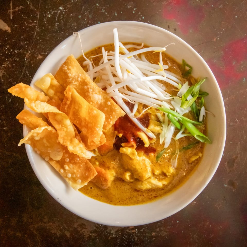 Overhead view of a bowl of yellow curry with chicken, bean sprouts, green onions, and crispy wontons.
