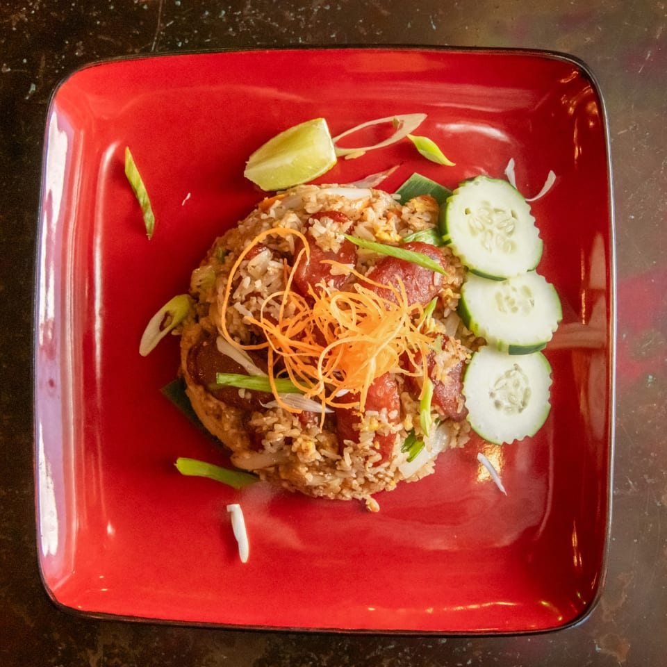 Fried rice with sliced sausage, shredded carrots, green onions, and cucumber on a red plate.