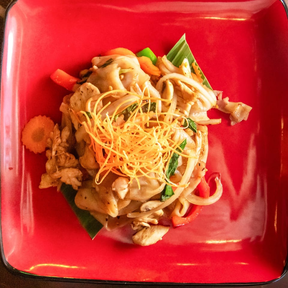 Pad See Ew with chicken, vegetables, and shredded carrots on a red square plate.