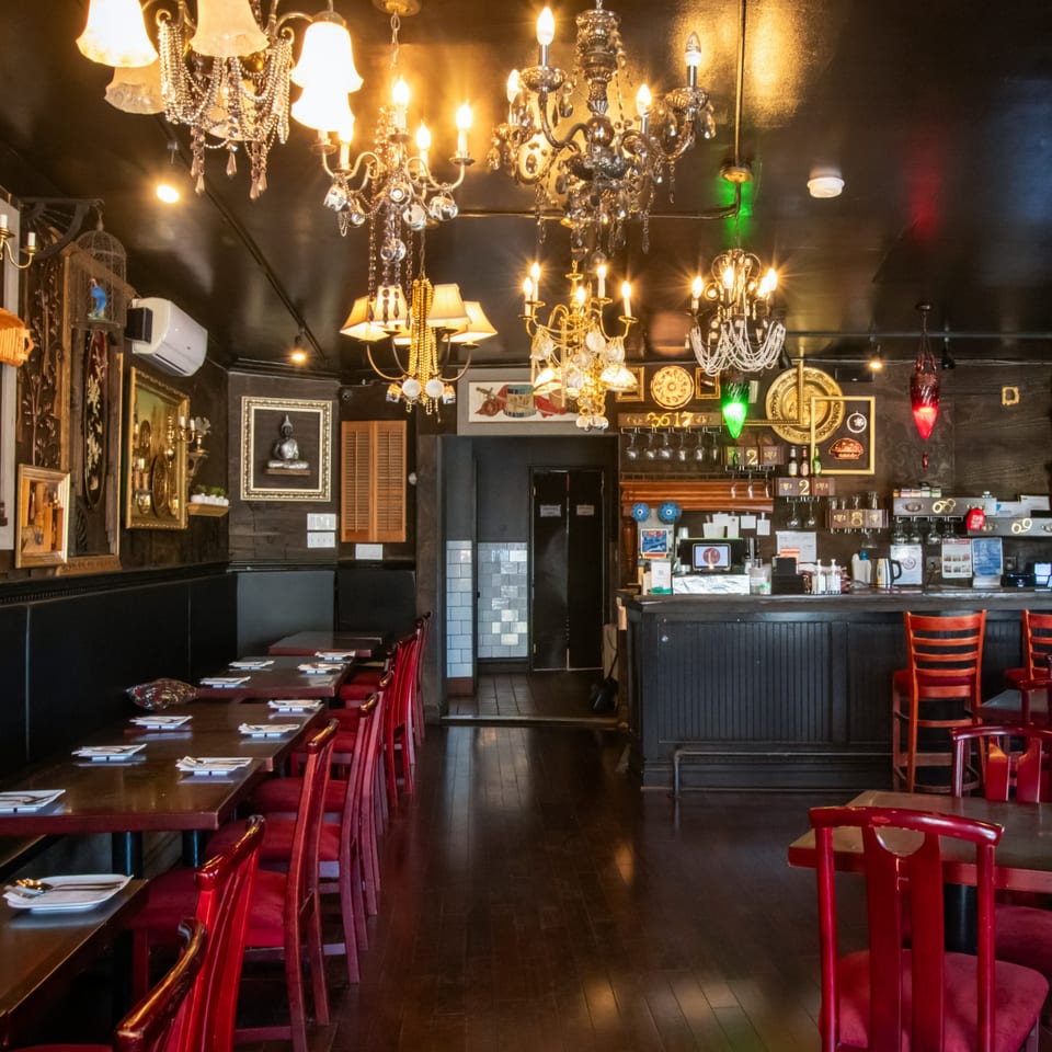 Restaurant interior with dark walls, red chairs, wooden tables, and ornate chandeliers.