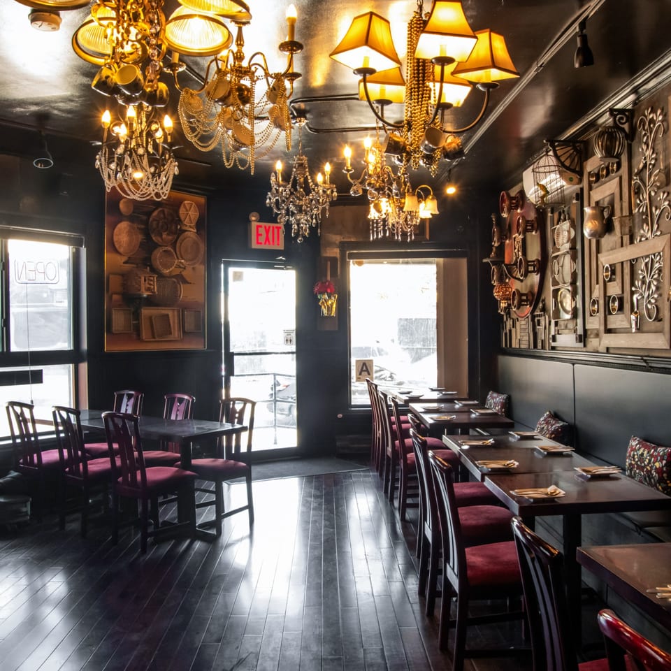A dark, ornate restaurant interior with chandeliers, red chairs, and set tables, bathed in warm light.